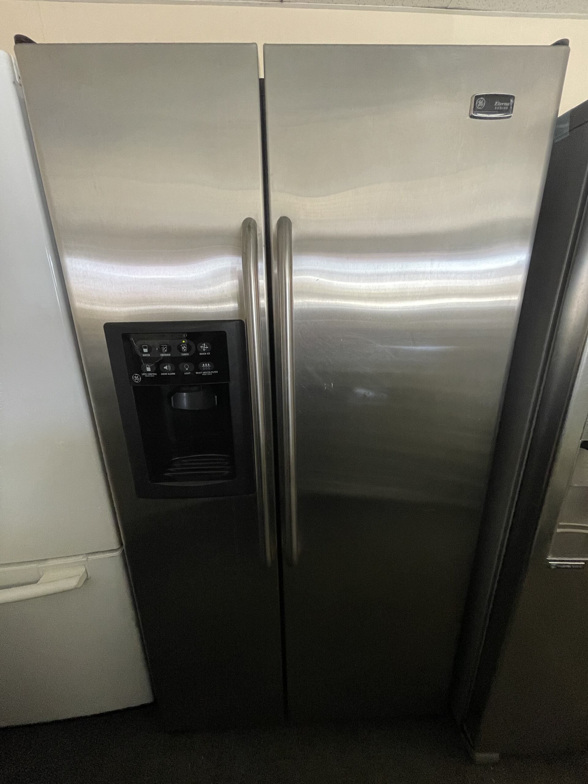 A stainless steel refrigerator is sitting next to a white refrigerator.