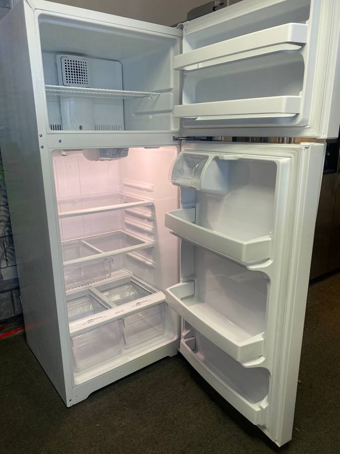 A white refrigerator with the door open is sitting on a carpet.