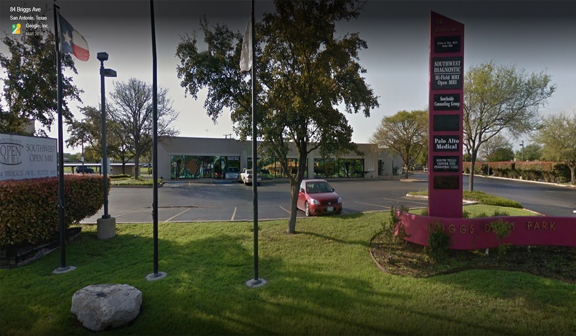 A red car is parked in a parking lot in front of a building.