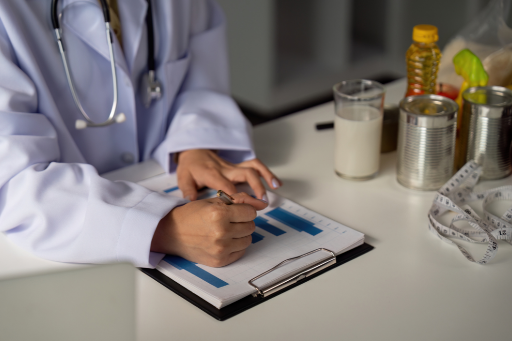 A doctor is sitting at a table writing on a clipboard.