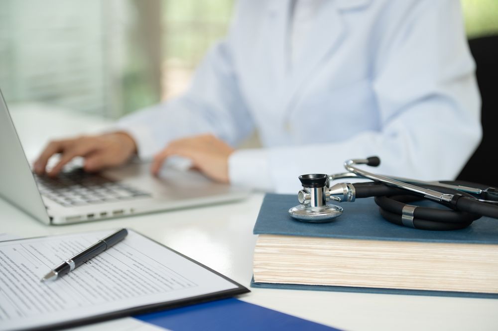 A doctor is sitting at a table writing on a clipboard.