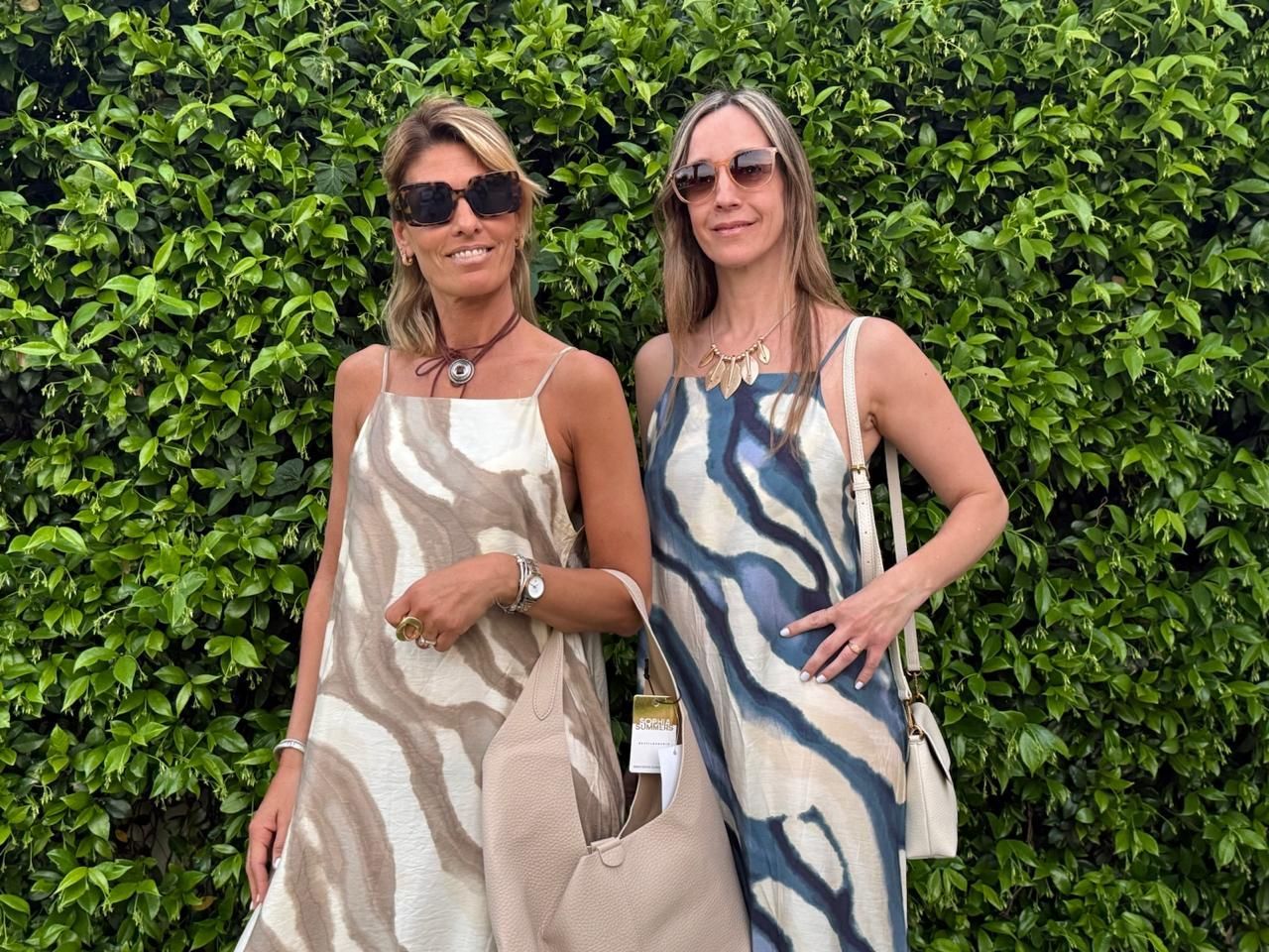 Dos mujeres con vestidos con estampado de cebra posan frente a un seto verde y llevan gafas de sol.