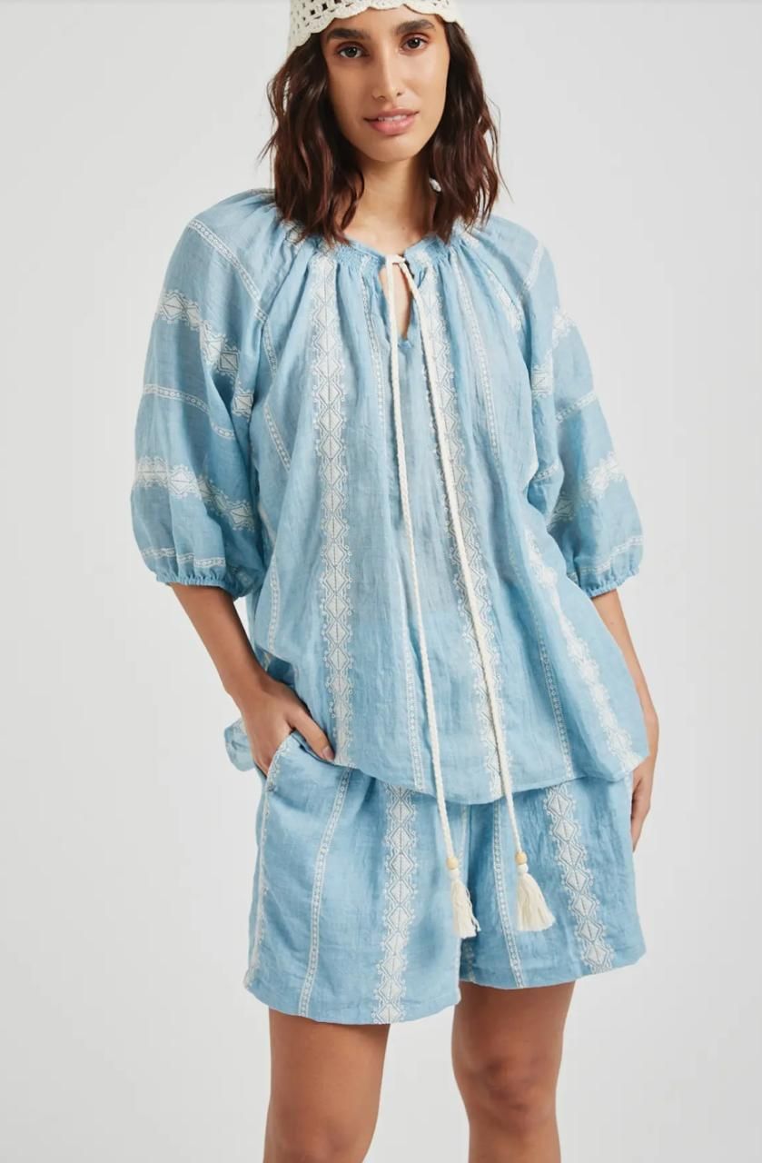 Mujer con un top tie-dye azul y pantalones cortos con un gorro de crochet, posando, con las manos en los bolsillos.