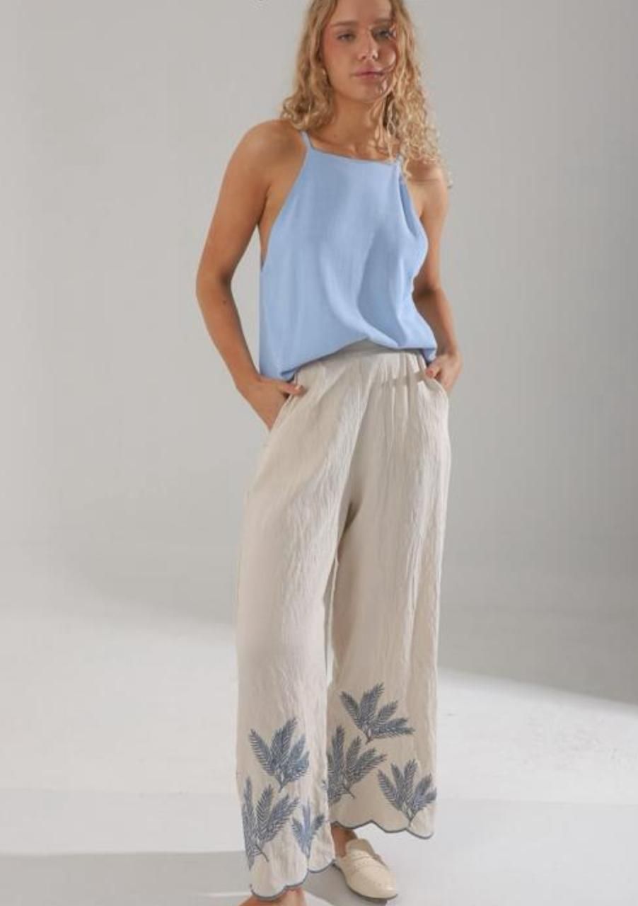 Mujer vestida con un top azul claro y pantalones color crema con bordado floral azul, posando en el interior.