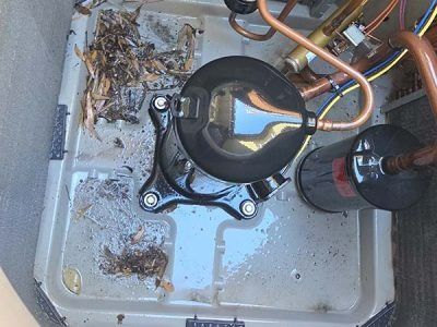 Dirty HVAC compressor unit with debris and copper tubing inside a metal cabinet