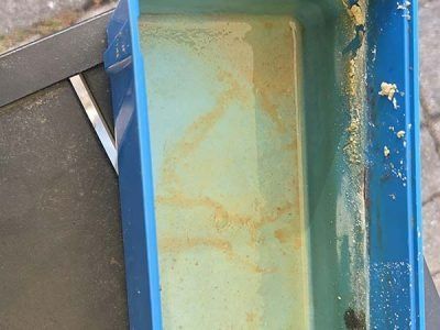Close-up of a blue plastic container with a pale green interior and visible rust stains.