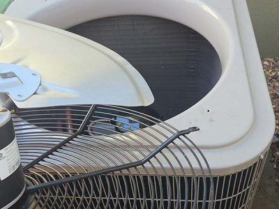 Damaged outdoor air conditioner unit with bent fan grille and detached top panel