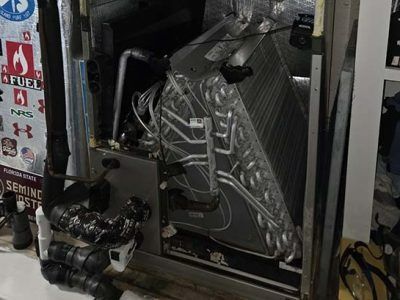 Wrapped industrial equipment in a metal frame, with cables and a printed plastic cover in a workshop.