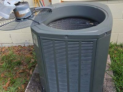 Outdoor HVAC condenser unit beside a brick house with a small vent cap on top