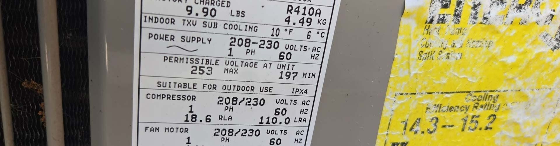 Close-up of a white equipment label beside a yellow sticker with handwritten numbers.