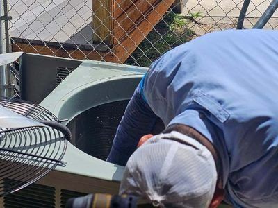 Worker in blue shirt inspecting an outdoor HVAC unit near a chain-link fence