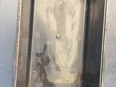 Close-up of a scratched metal surface with dark stains and small rivets.