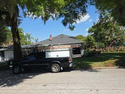 Black pickup truck parked in front of a single-story suburban house under trees on a sunny day