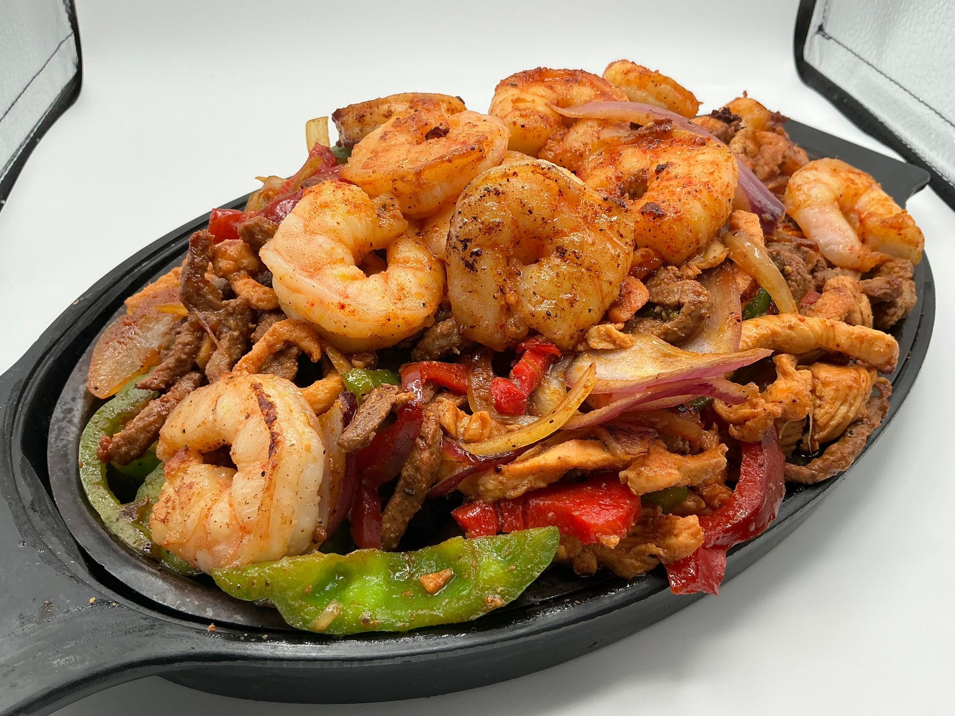 Sizzling platter of shrimp, chicken, and vegetables (peppers, onions) seasoned with spices.