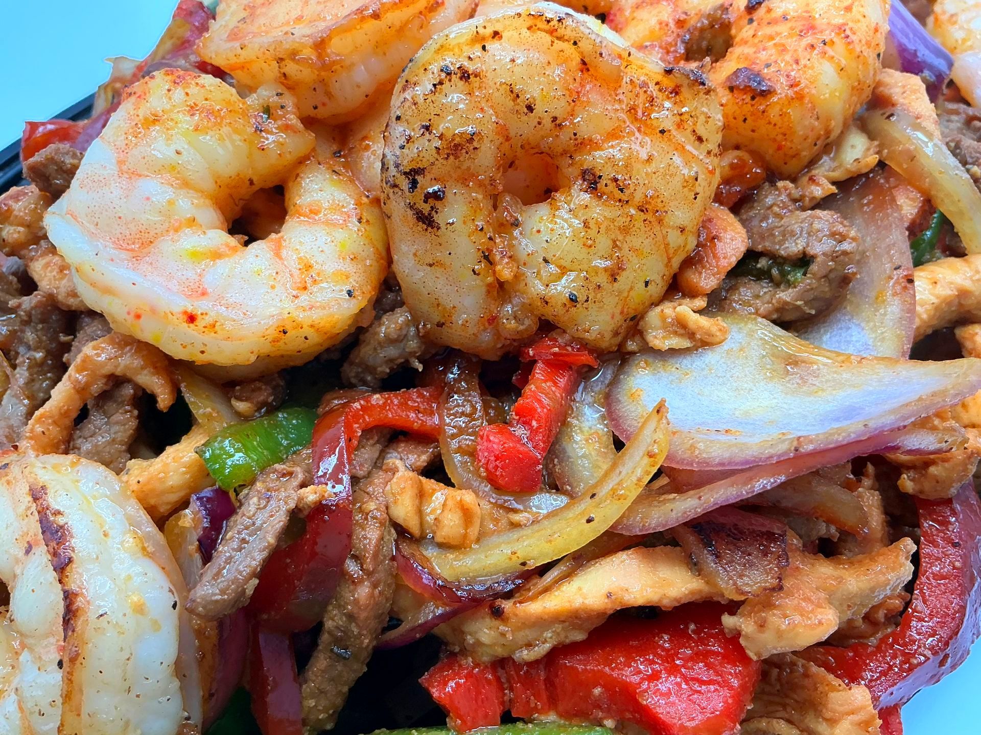 Sizzling fajitas: grilled shrimp, steak, onions, and bell peppers in a dish.