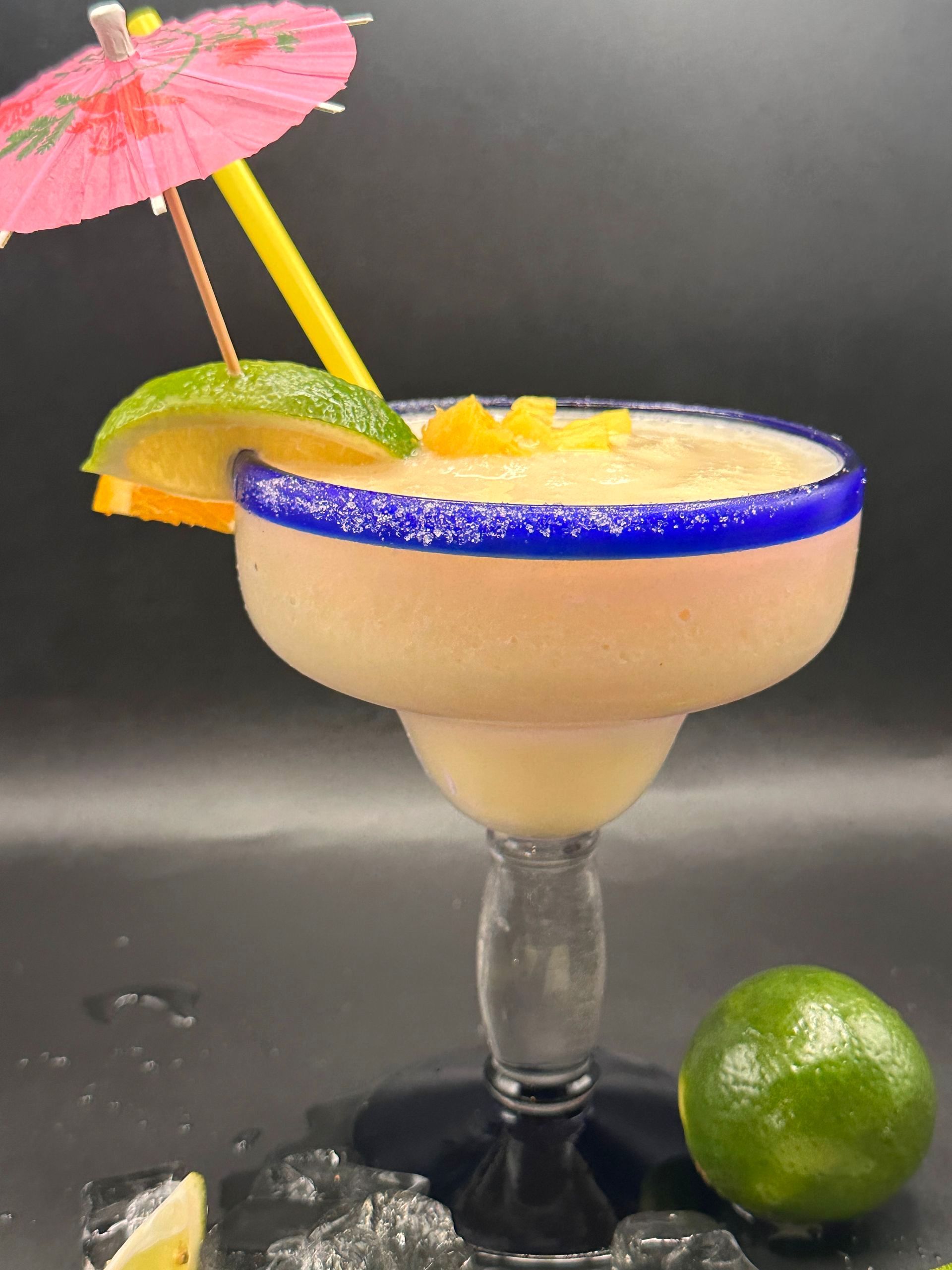 Frozen mango margarita garnished with lime, orange, and umbrella in a margarita glass.