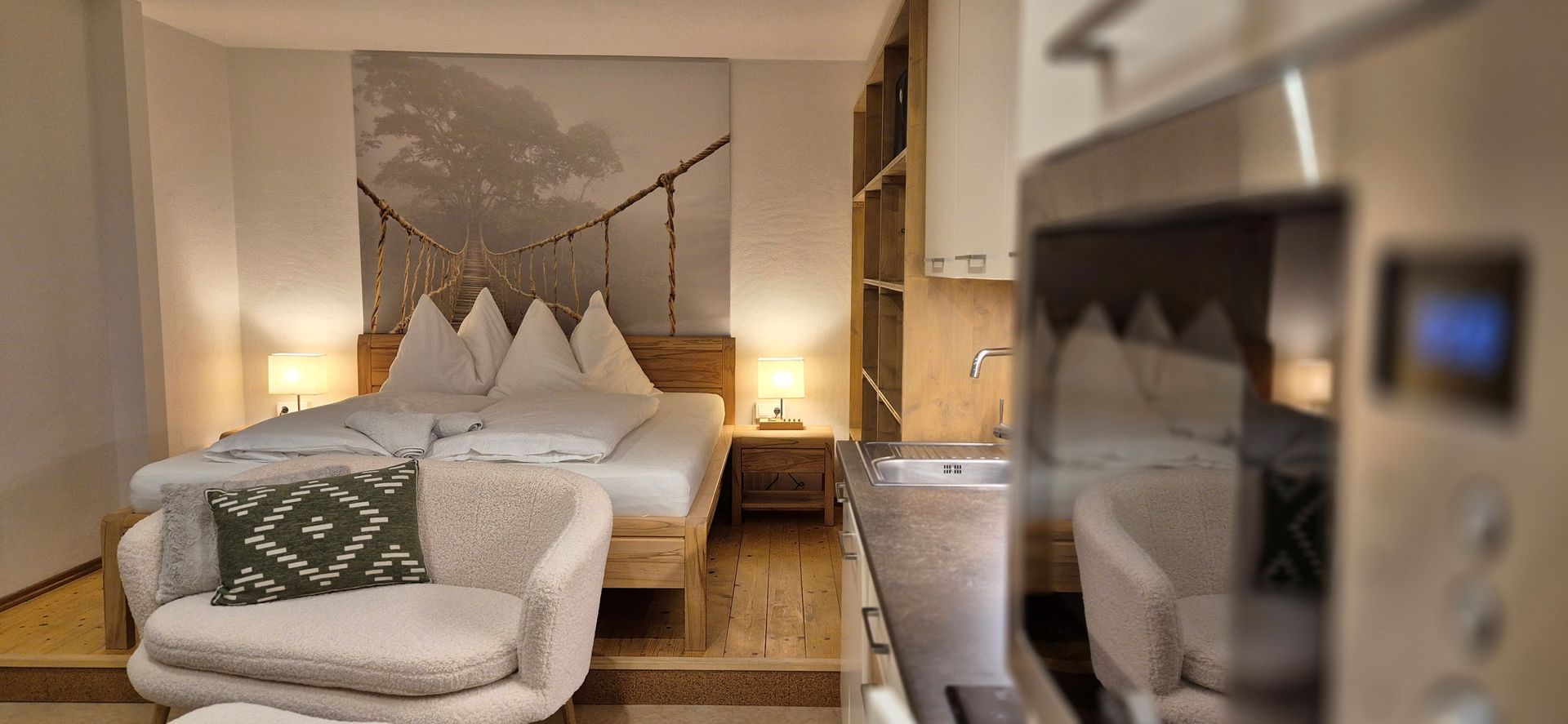 Modernes Hotelzimmer mit Bett, Sessel, warmer Beleuchtung und einem eleganten Badezimmerspiegel im Vordergrund