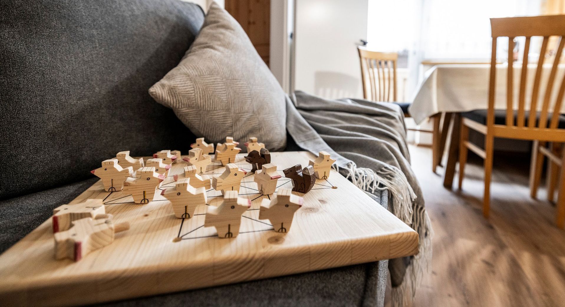 Auf einem Couchtisch neben einem grauen Sofa und Kissen liegt ein angefangenes Puzzle; im Hintergrund sind Esszimmerstühle zu sehen.