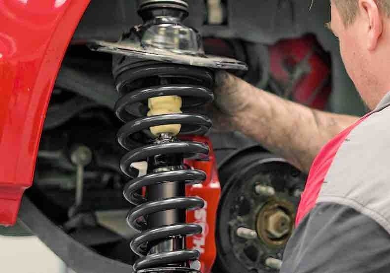 A Man is Working on a Shock Absorber on a Car — K & T Ballina Mechanical In Ballina, NSW