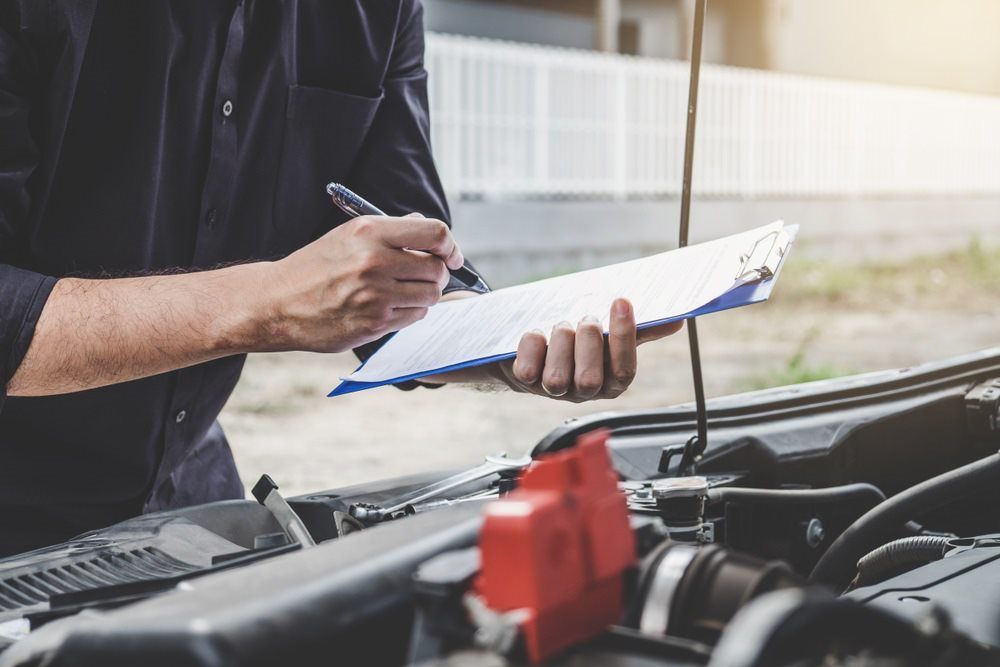 A Man is Writing on a Clipboard While Standing Next to a Car — K & T Ballina Mechanical In Ballina, NSW