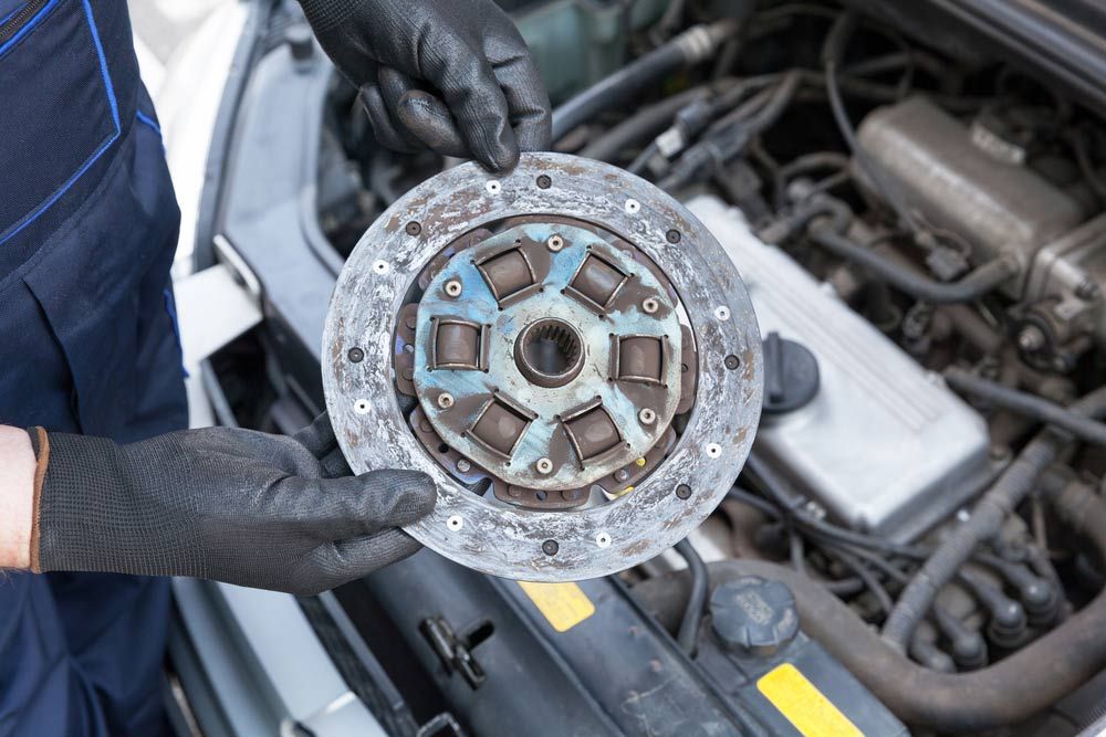 A Person is Holding a Clutch Disc in Front of a Car Engine — K & T Ballina Mechanical In Ballina, NSW