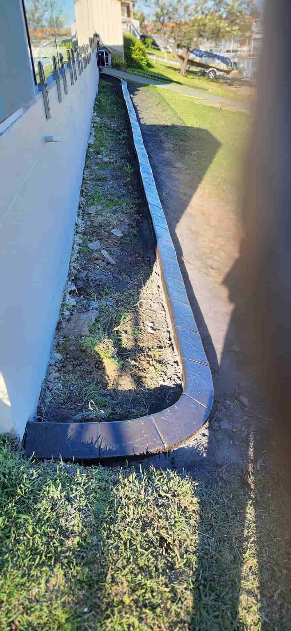 A Narrow Garden Bed Bordered by a Winding Dark Border — Brett Continuous Concrete Kerbing & Edging In Wauchope, NSW