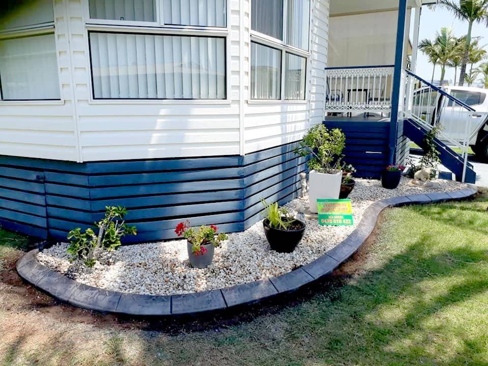 A Neatly Landscaped Garden Borders a White and Blue House — Brett Continuous Concrete Kerbing & Edging In Lakewood, NSW