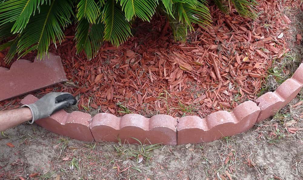 A Person in a Glove Arranges Red Scalloped Garden Edging — Brett Continuous Concrete Kerbing & Edging In Lakewood, NSW