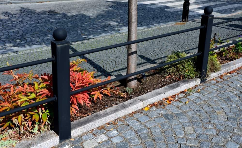 A Black Metal Railing in a Cobblestone Sidewalk — Brett Continuous Concrete Kerbing & Edging In Lakewood, NSW