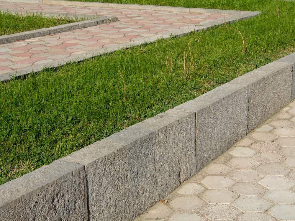 A Garden Bed Bordered by Gray Stone Bricks — Brett Continuous Concrete Kerbing & Edging In Lake Cathie, NSW