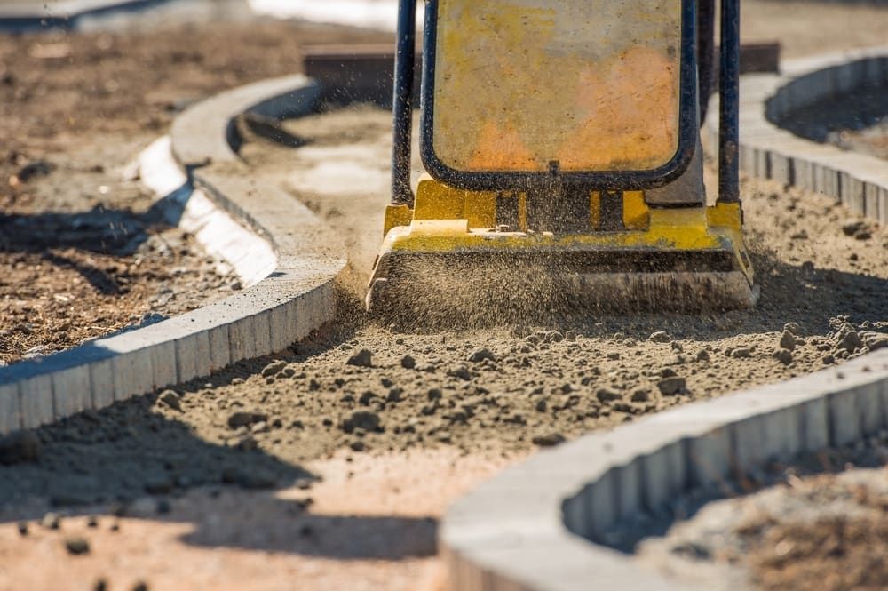 A Yellow Plate Compactor Smoothing Gravel Between Curved Borders — Brett Continuous Concrete Kerbing & Edging In Laurieton, NSW