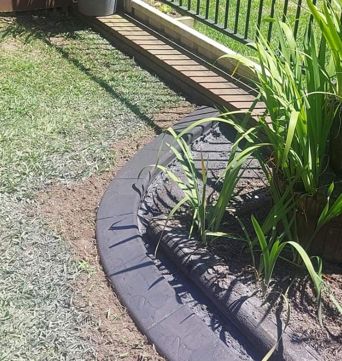 Curved Garden Bed Bordered by Black Stone Pavers — Brett Continuous Concrete Kerbing & Edging In Wauchope, NSW