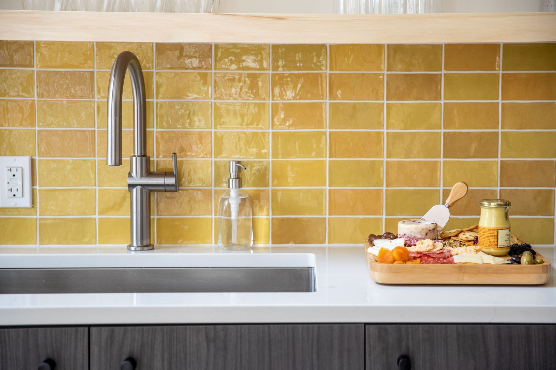 A kitchen with yellow tiles , a sink , and a cutting board.