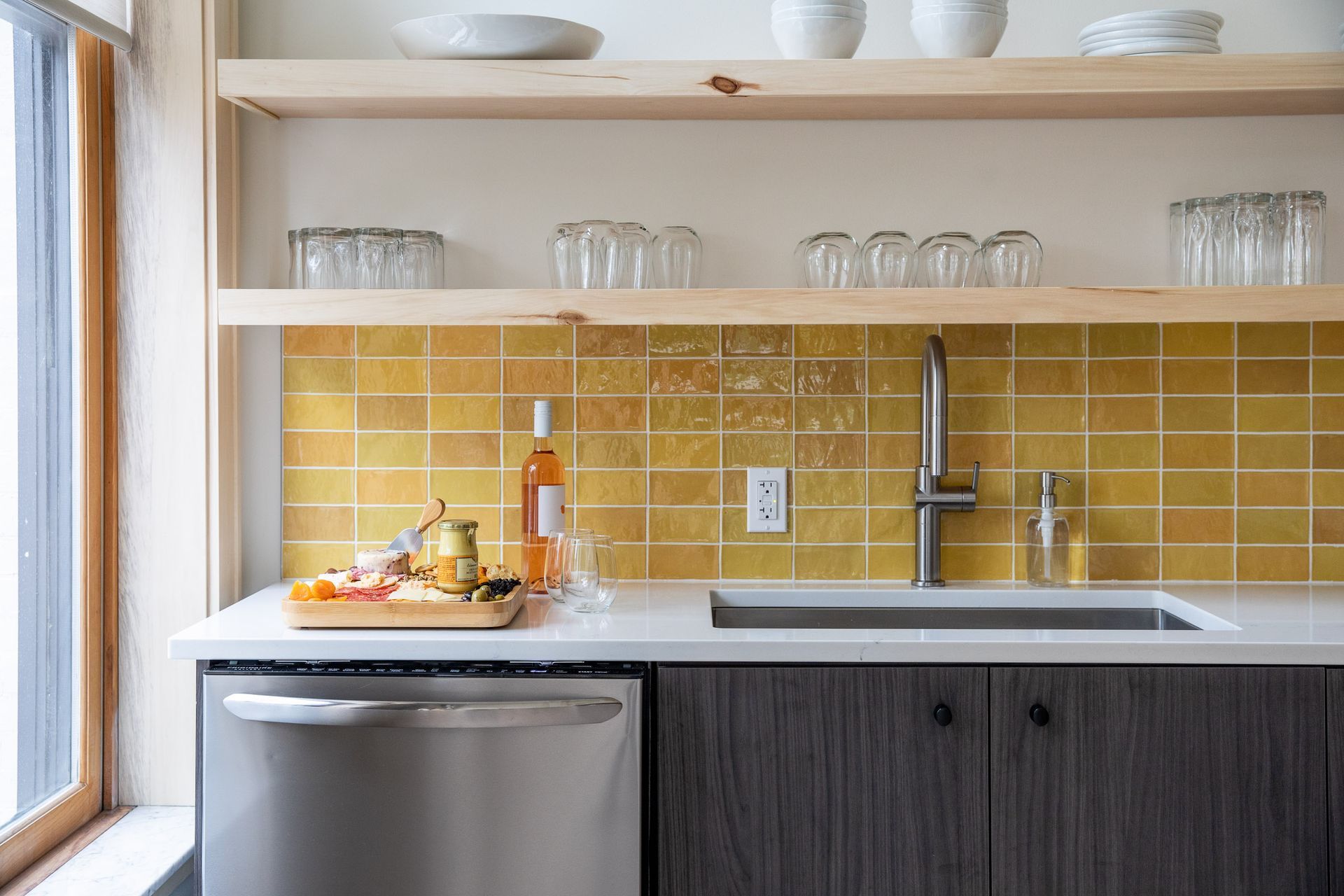 A kitchen with yellow tiles , a sink , a dishwasher , and a window.