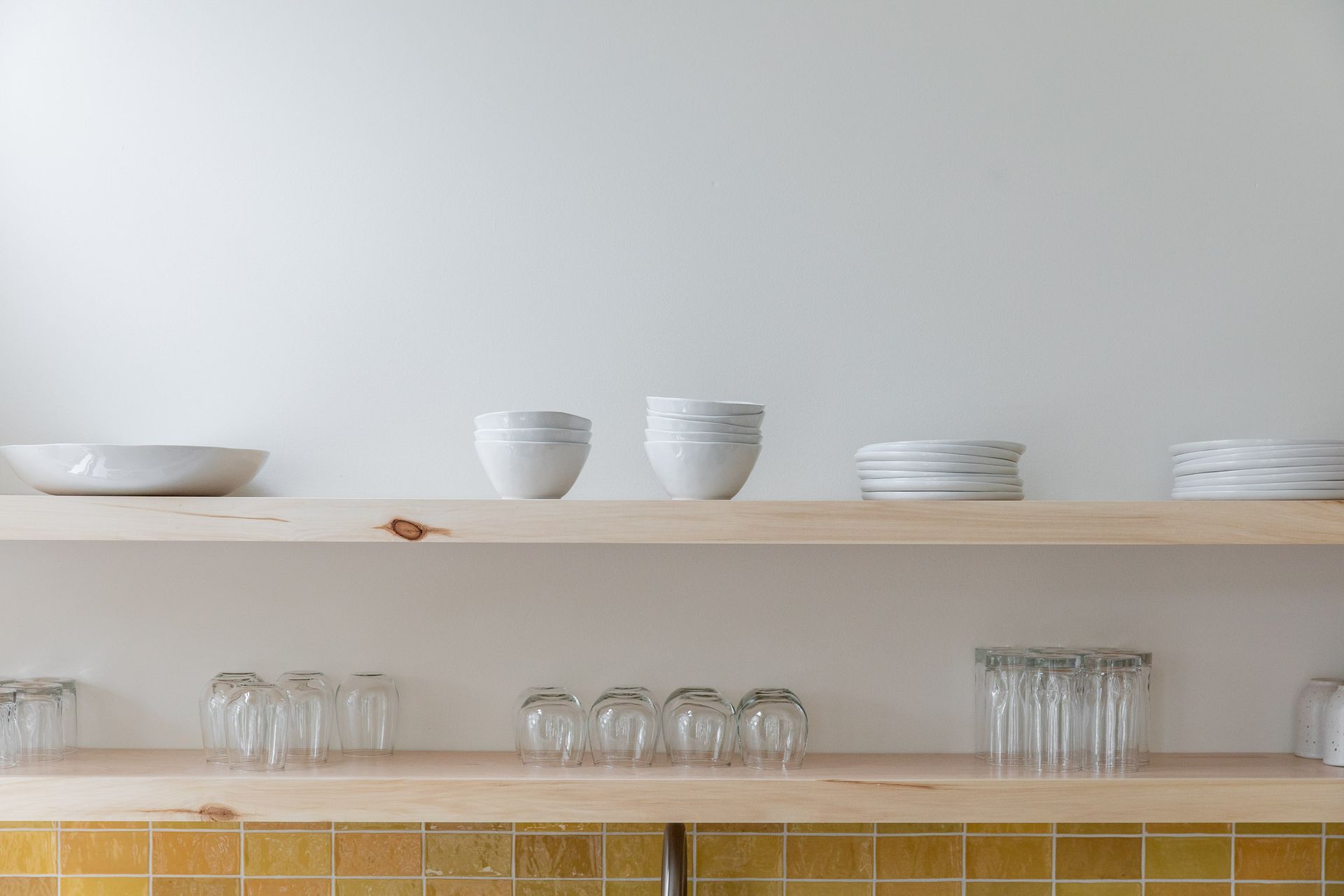 A wooden shelf with plates and glasses on it in a kitchen.
