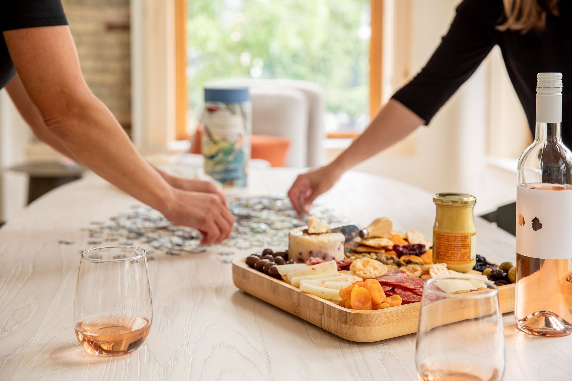 A couple is sitting at a table with a bottle of wine and a tray of food.