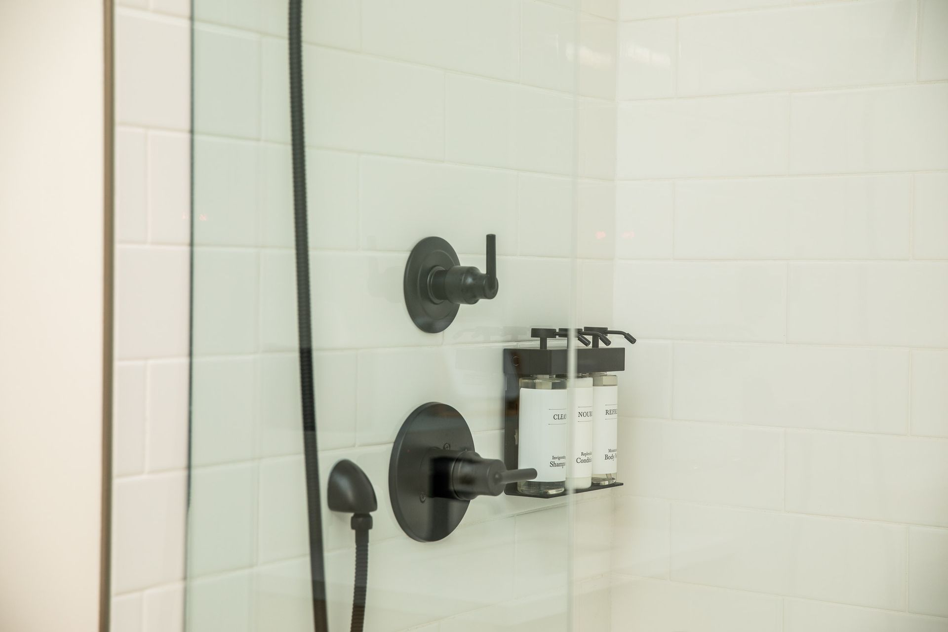 A shower with a glass door and two soap dispensers on the wall.
