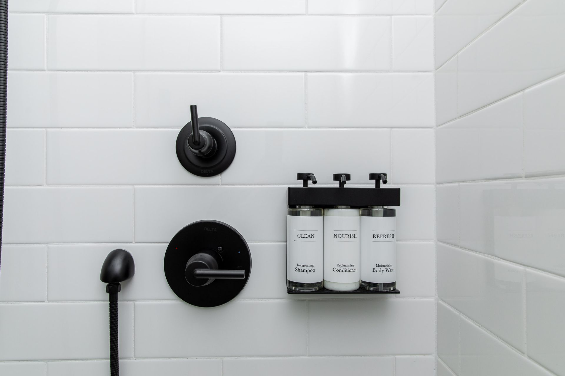A shower with three bottles of shampoo and conditioner hanging on the wall.