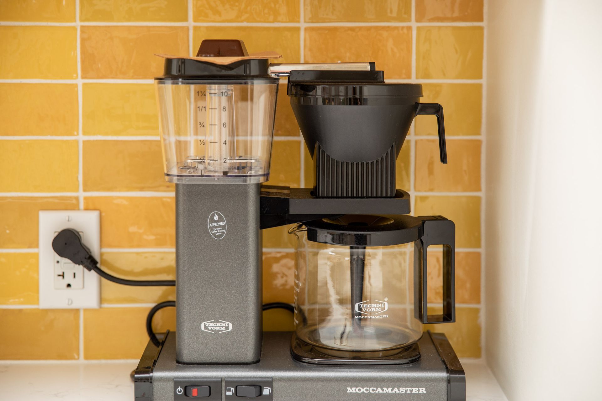 A coffee maker is sitting on a counter next to a yellow tiled wall.