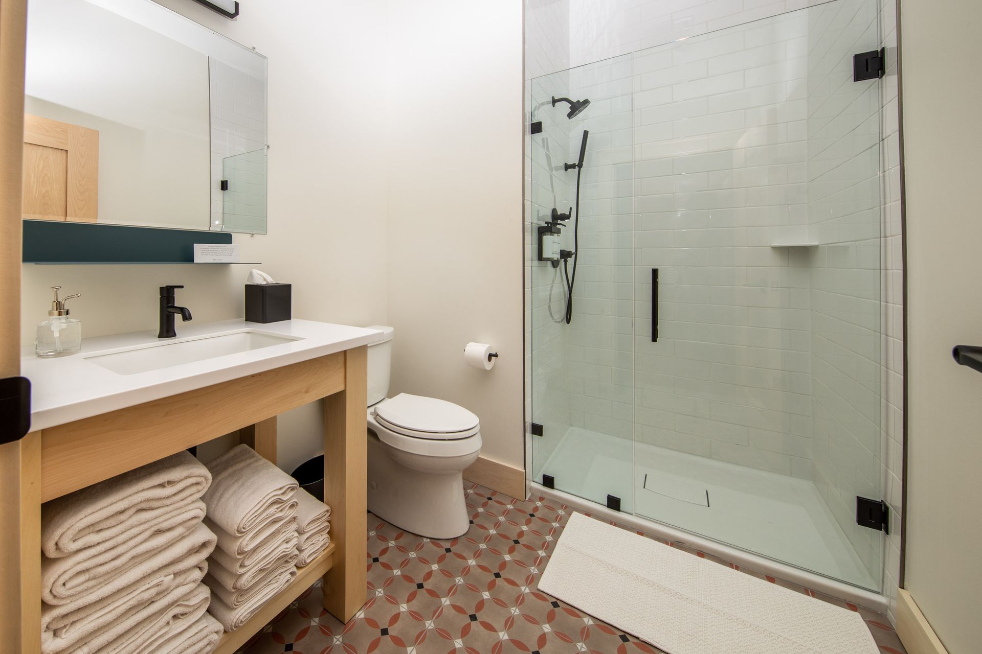 A bathroom with a toilet , sink , mirror and walk in shower.