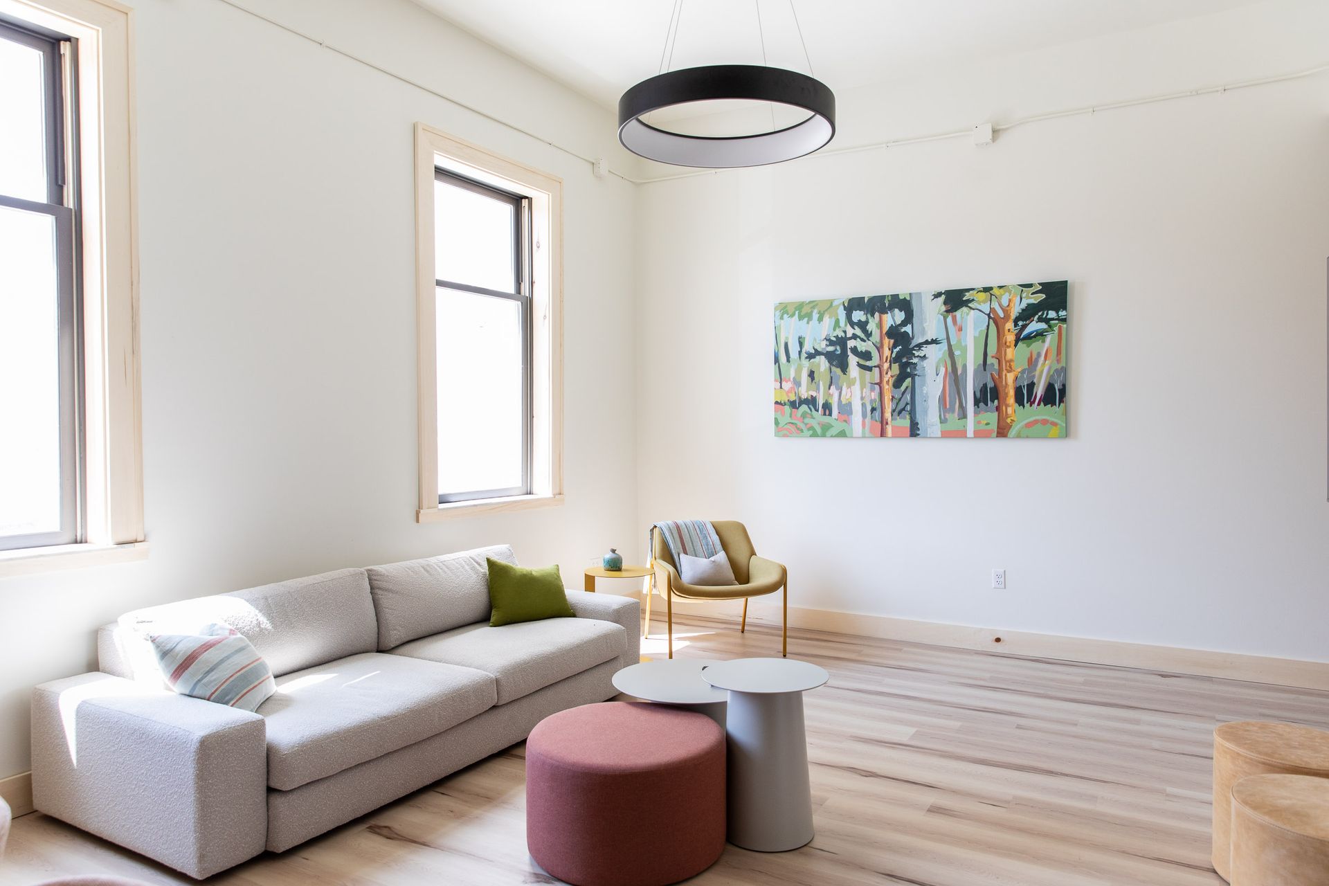 A living room with a couch , chairs , ottomans and a painting on the wall.