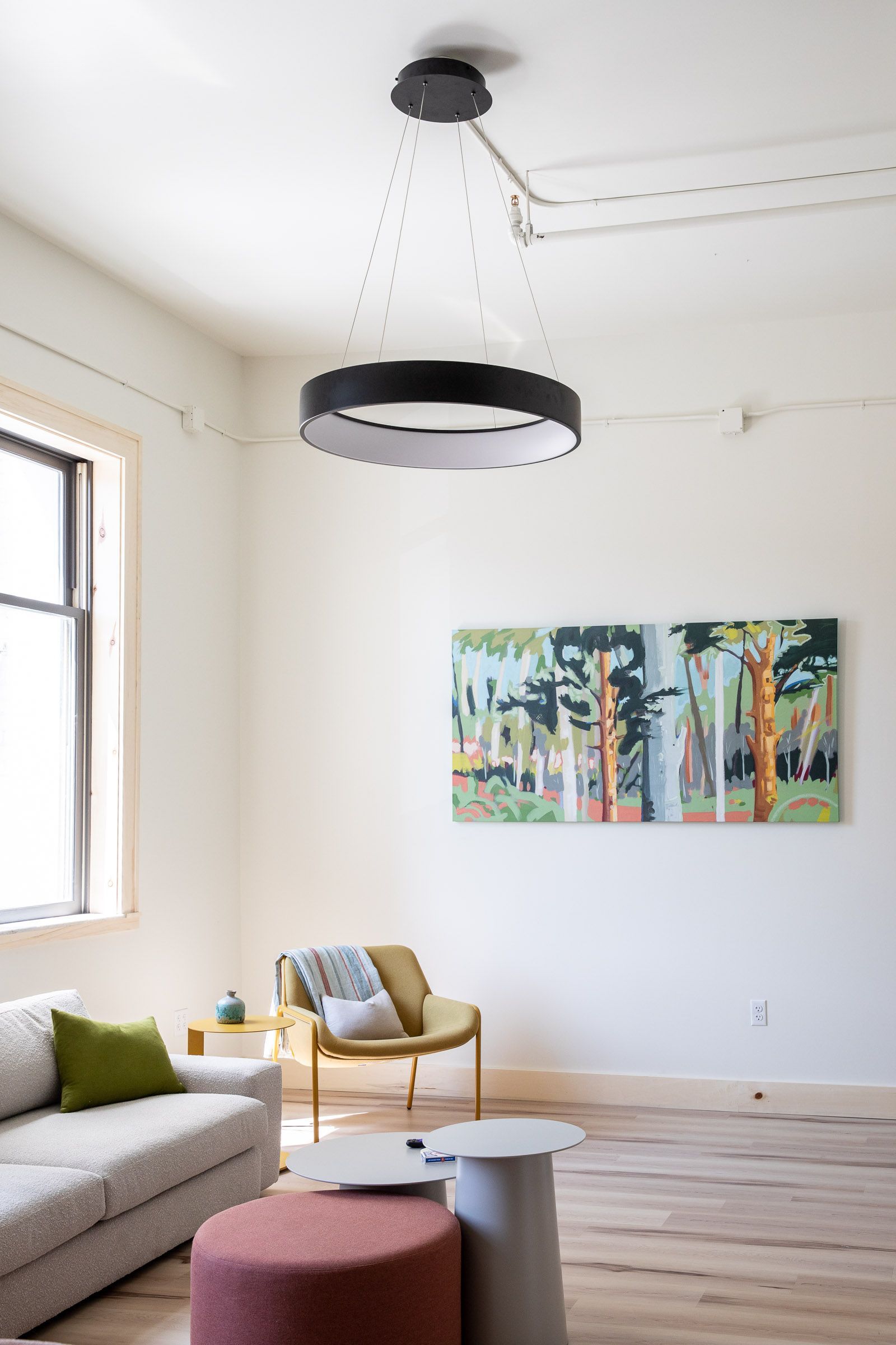 A living room with a couch , chair , ottomans and a painting on the wall.
