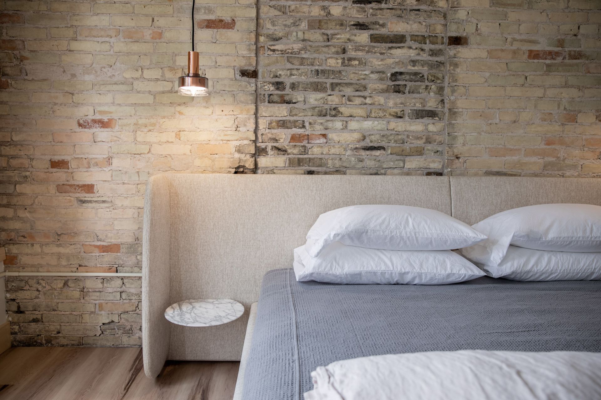 A bed with white sheets and pillows in a bedroom with a brick wall.