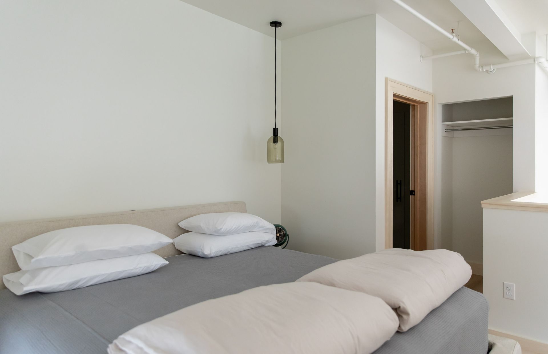 A bedroom with a bed , pillows , and a light hanging from the ceiling.