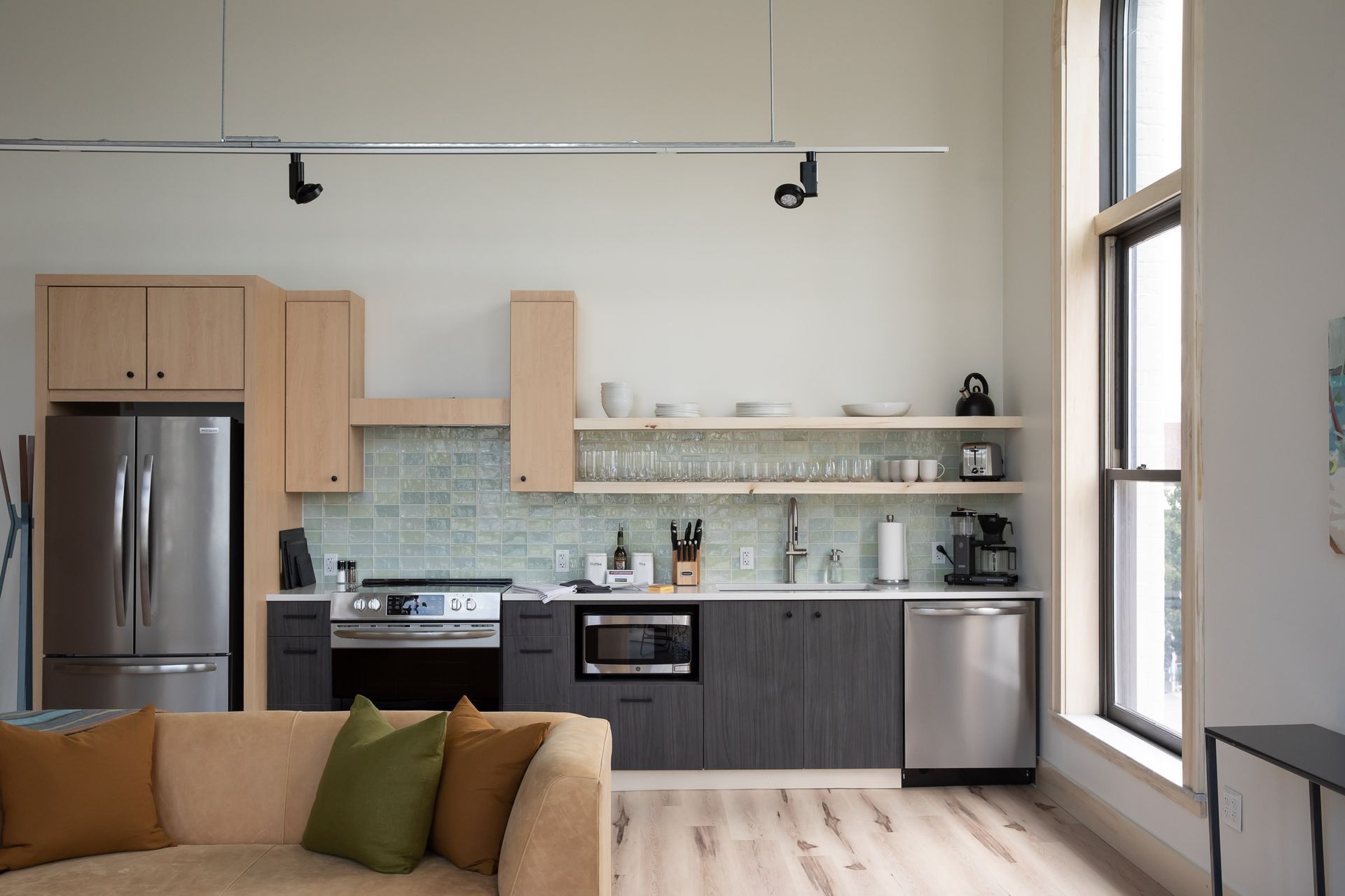 A living room with a couch and a kitchen with stainless steel appliances