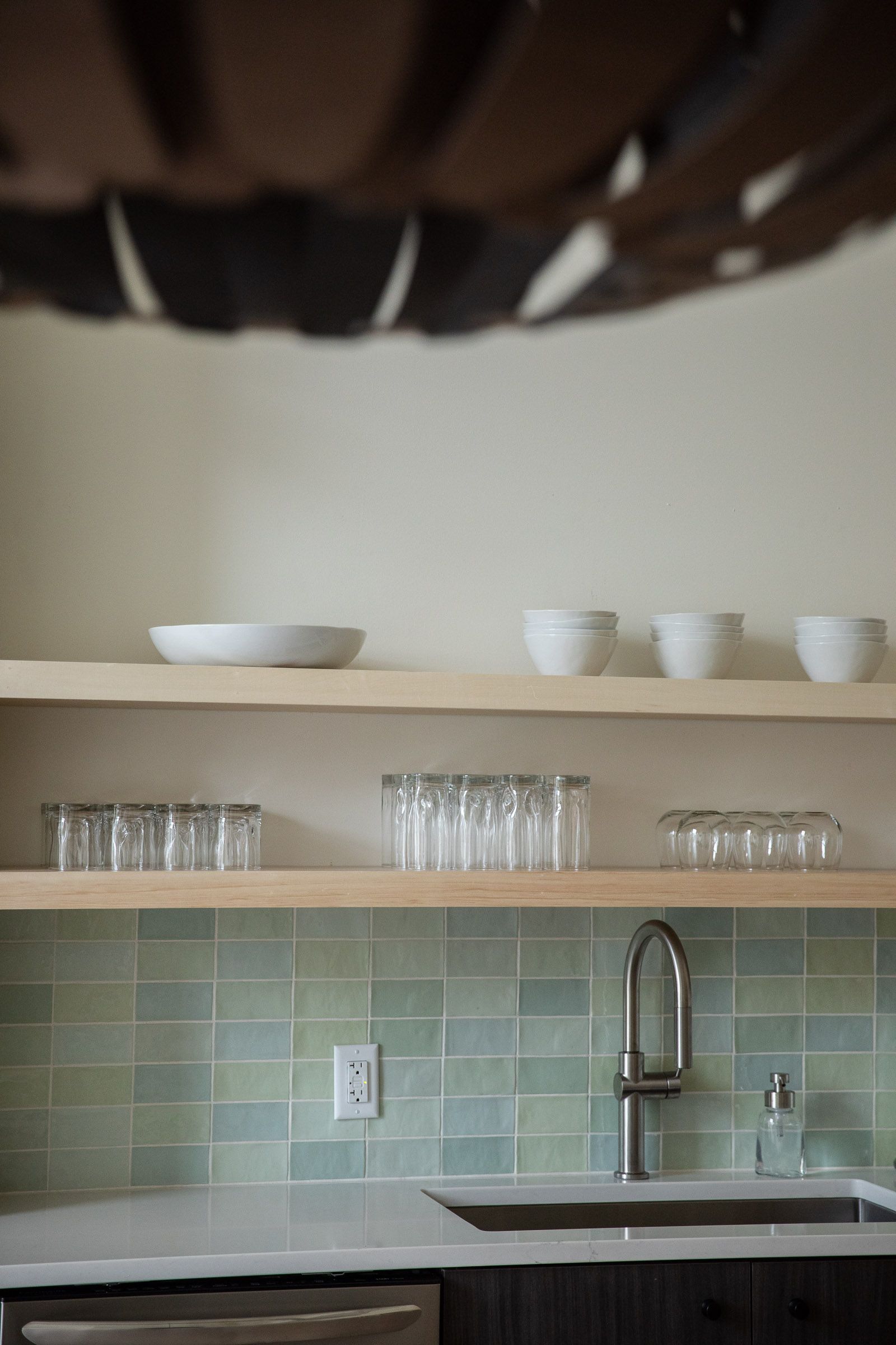 A kitchen with a sink and shelves filled with bowls and glasses