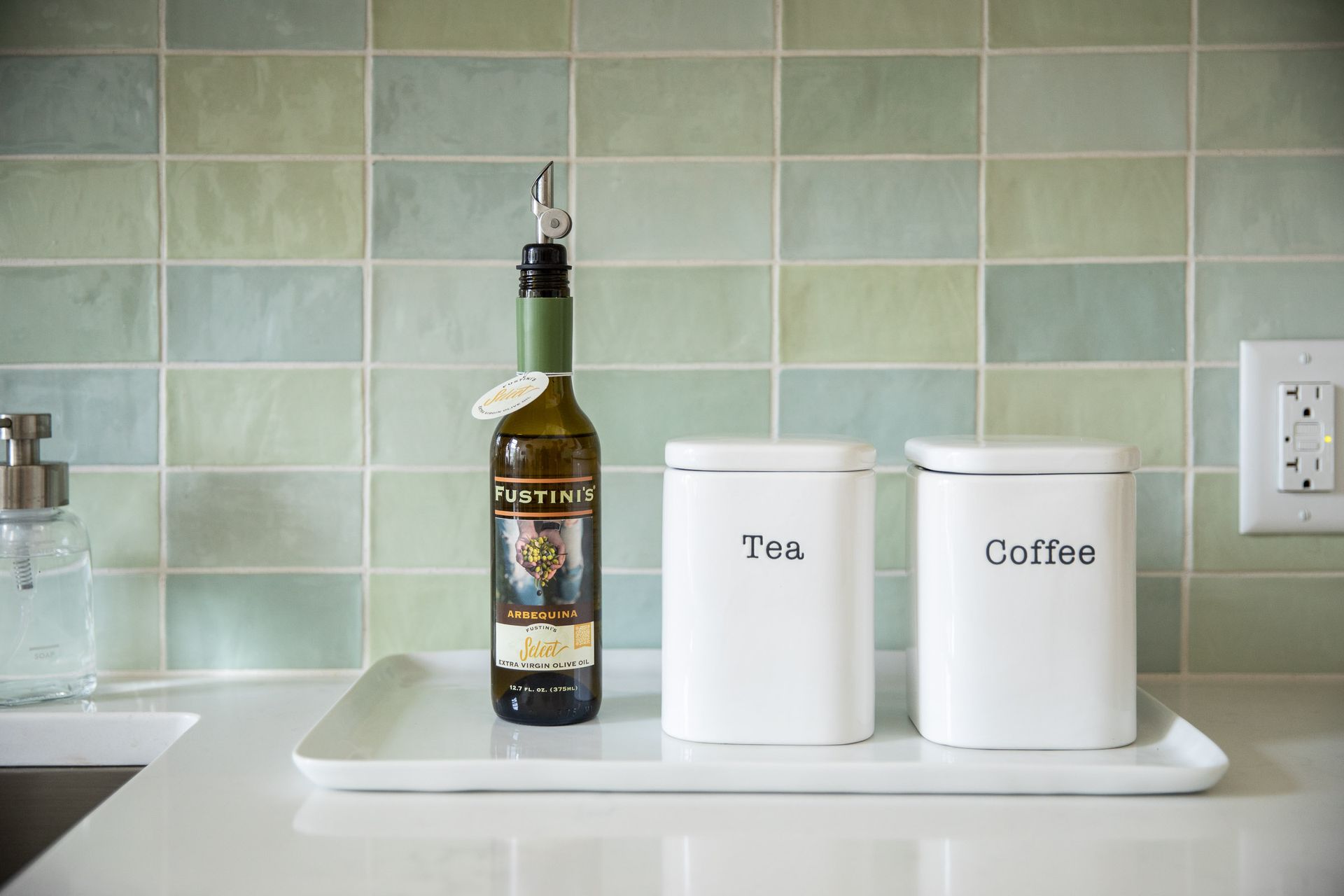 A bottle of wine sits on a tray next to tea and coffee canisters