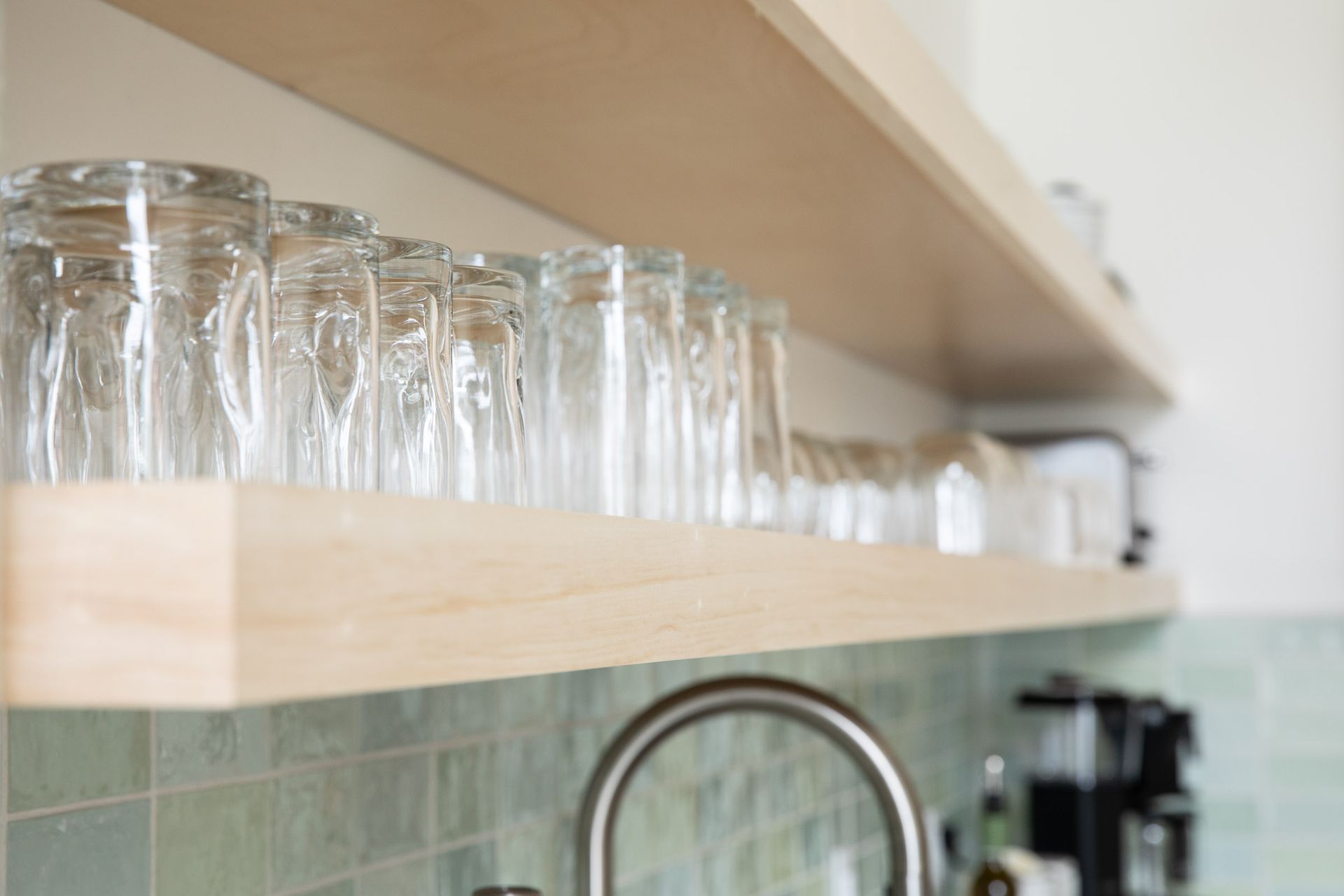 A kitchen with a sink and a shelf with glasses on it