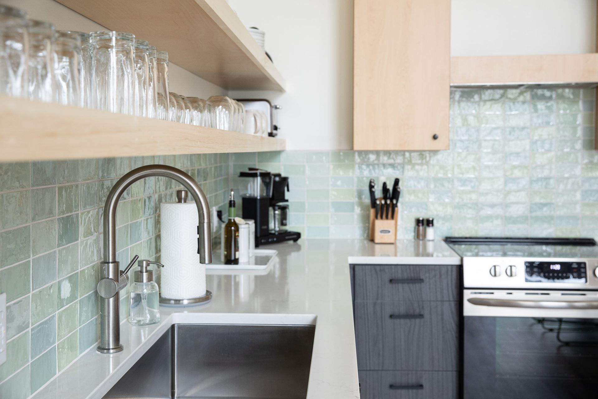 A kitchen with a sink , stove , and shelves filled with glasses.