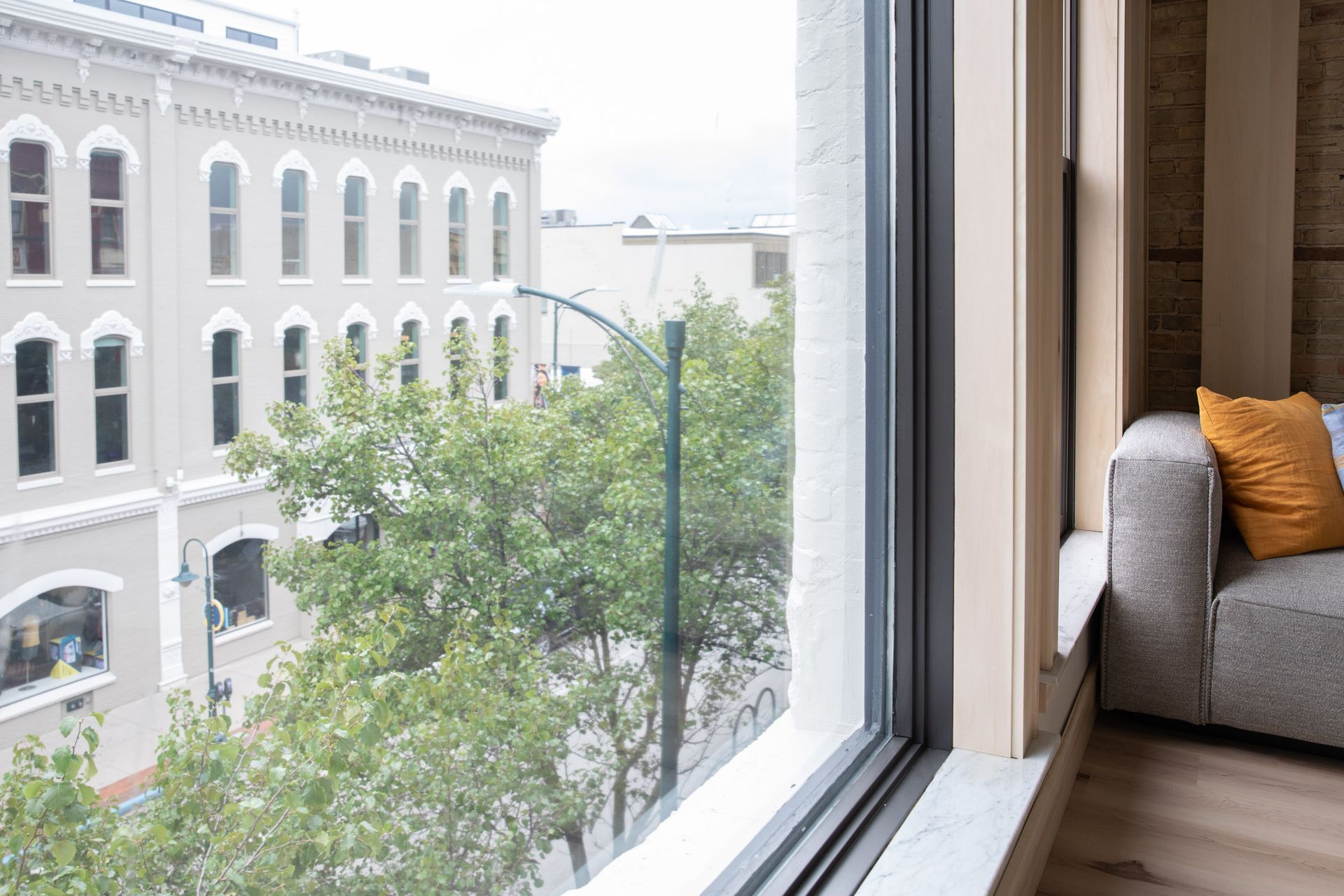 A living room with a couch and a large window with a view of a city street.